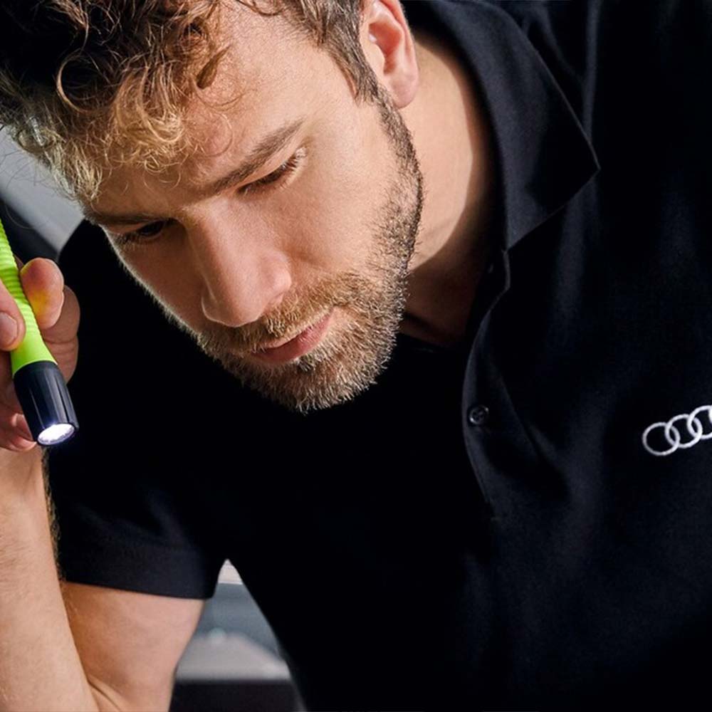 Mann untersucht mit Taschenlampe Motorraum