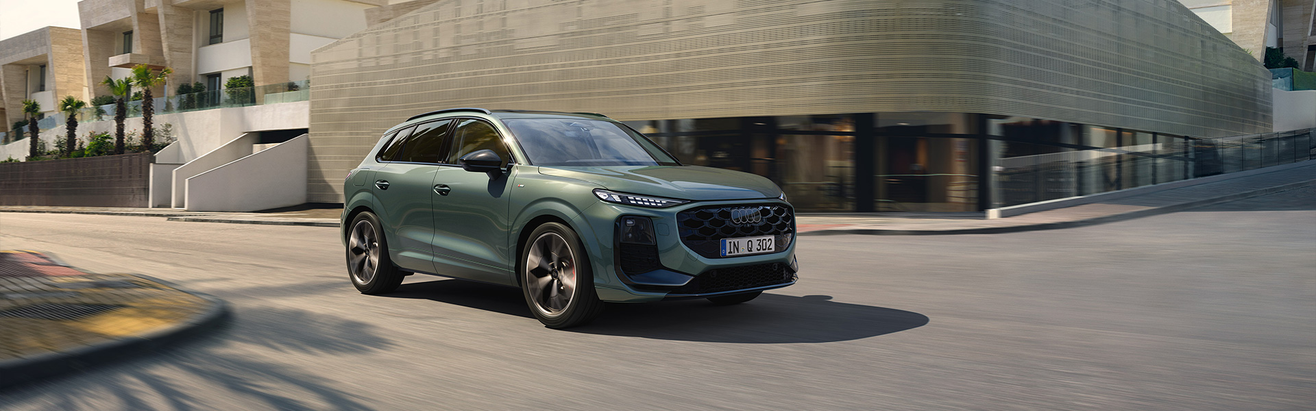 Audi Q3 f&auml;hrt auf Sta&szlig;e vor einem modernen Geb&auml;ude. 