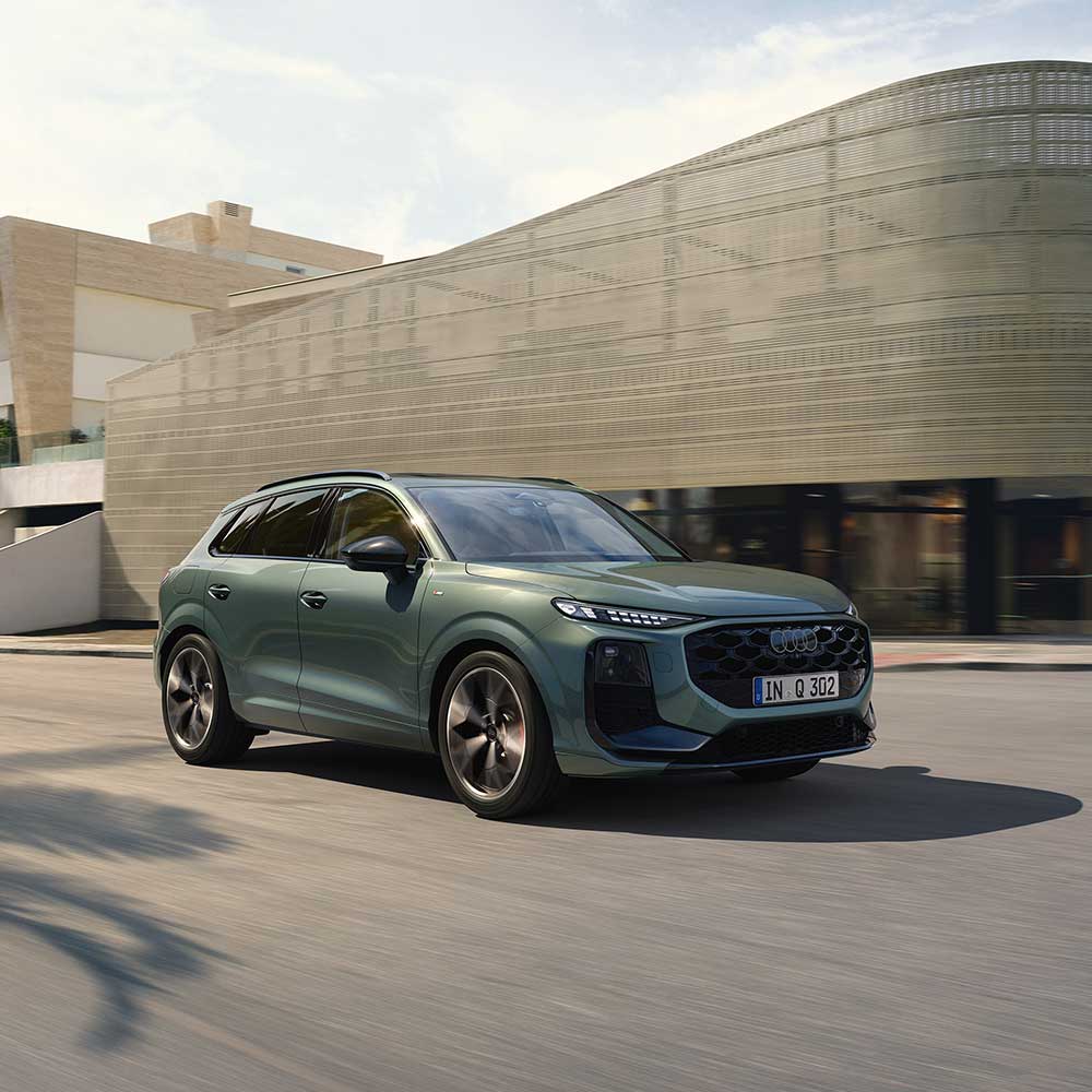 Audi Q3 f&auml;hrt auf Sta&szlig;e vor einem modernen Geb&auml;ude. 